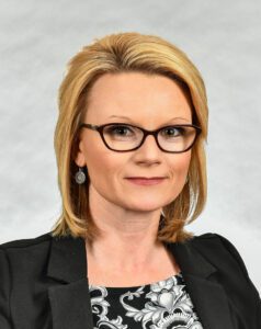 A woman with glasses and blonde hair wearing a black jacket.