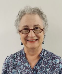A woman with glasses and grey hair wearing a blue shirt.
