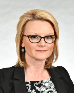 A woman with glasses and blonde hair wearing a black jacket.