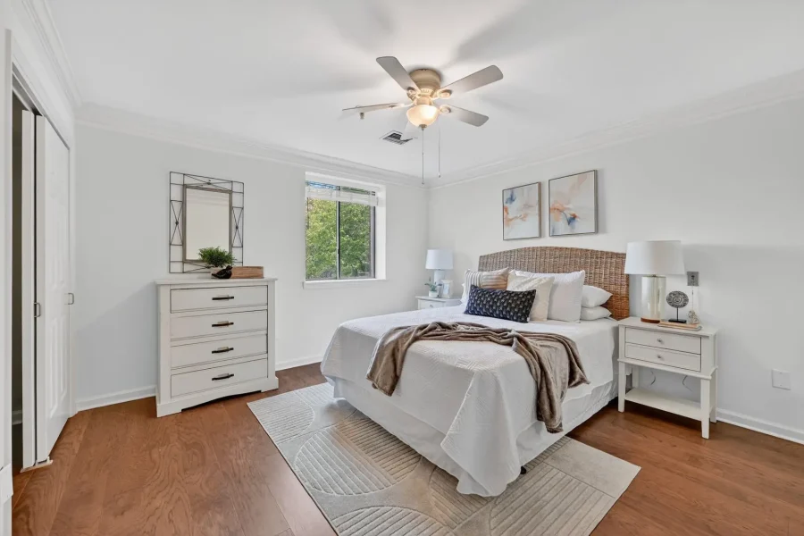 Bright white bedroom with a wicker headboard bed, two white nightstands, and a ceiling fan in a sunlit room.