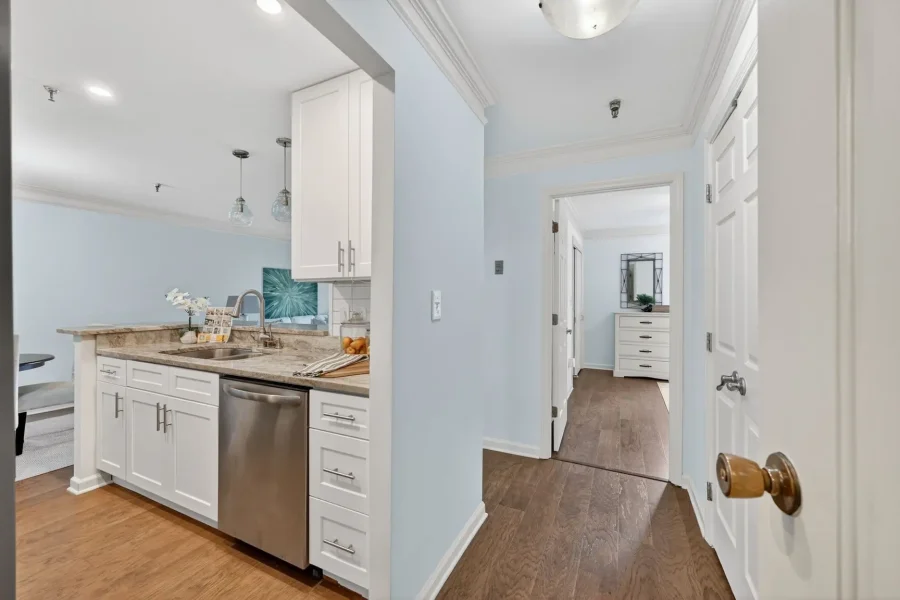 Open-concept kitchen with white cabinets, granite countertop, stainless dishwasher, and light blue walls; pendant lights above the island.
