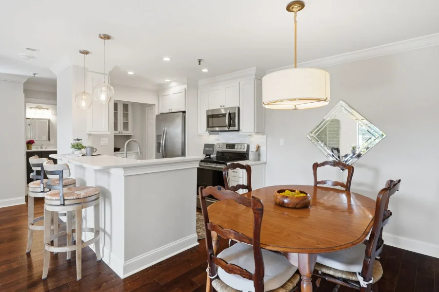 Bright open kitchen and dining area with white cabinets, stainless steel appliances, and a round wooden dining table with carved chairs.