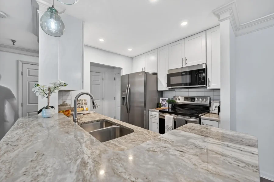 Contemporary kitchen with white cabinets, stainless appliances, and a marble countertop island with a double sink.