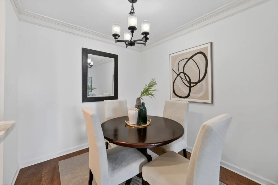 Dining room with a round dark wood table and four cream upholstered chairs under a hanging chandelier, with abstract wall art and a mirror.