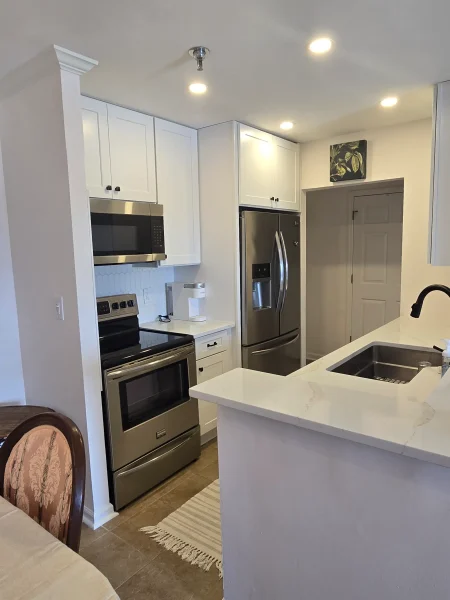 Modern kitchen with white cabinets and stainless steel fridge, microwave, and oven, plus a marble-like island counter with a sink.
