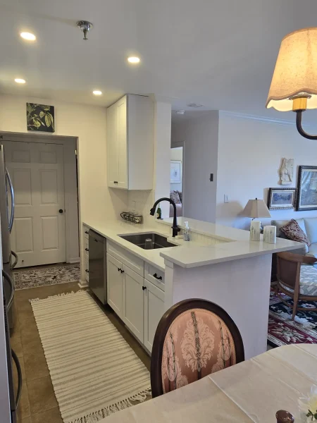 Bright white kitchen with an island, black faucet, and built-in appliances under recessed ceiling lights.