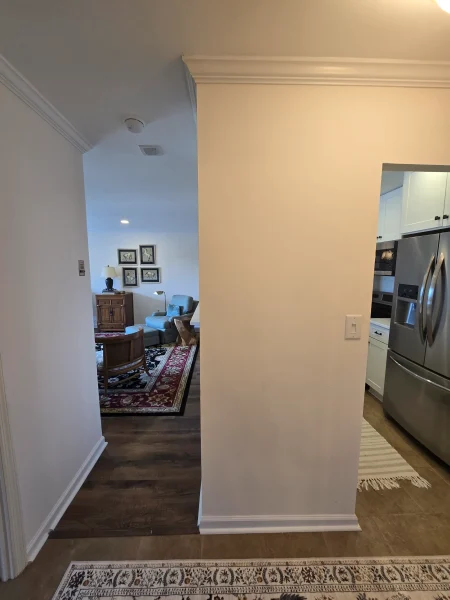view of a hallway opening into a living room with a red-patterned rug, wooden furniture, and light walls