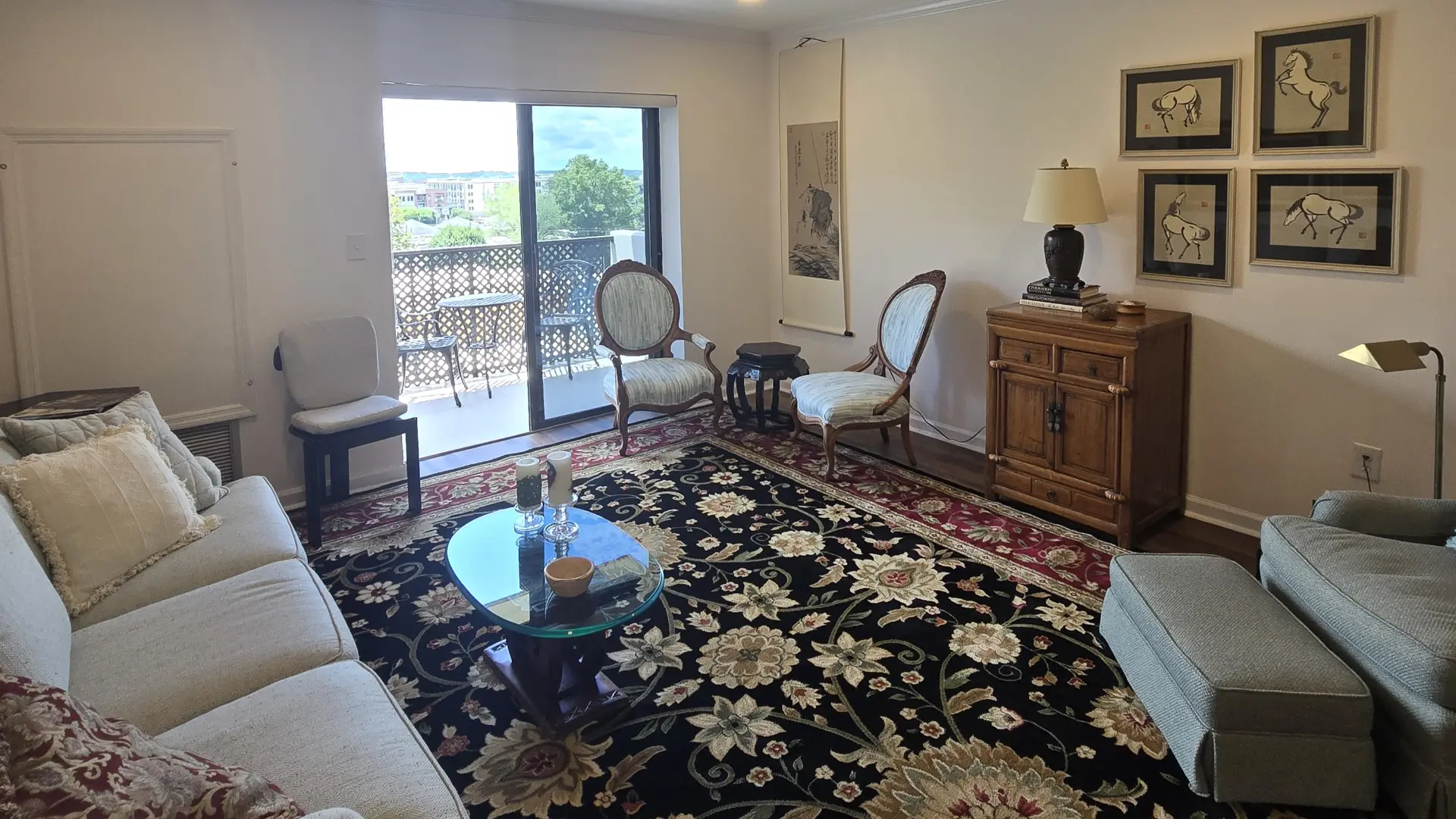 Cozy living room with beige sofa, patterned rug, glass coffee table, and vintage oval chairs near a sliding balcony door.