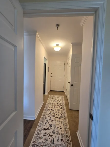 Narrow hallway with white walls and crown molding, a long patterned runner rug leading to a white front door at the end.