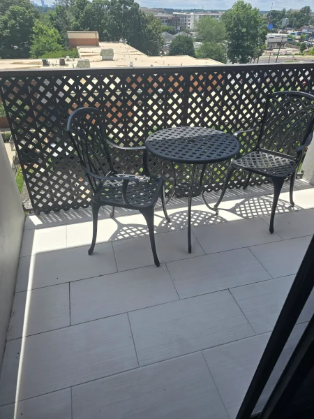 Balcony set with a round perforated table and two matching chairs, casting geometric shadows on light floor with a cityscape in the background.