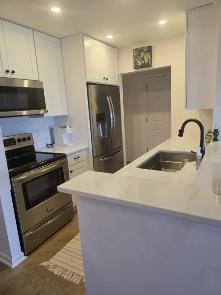 Modern kitchen with white cabinets, stainless steel fridge and range, and a marble-topped island with a sink.
