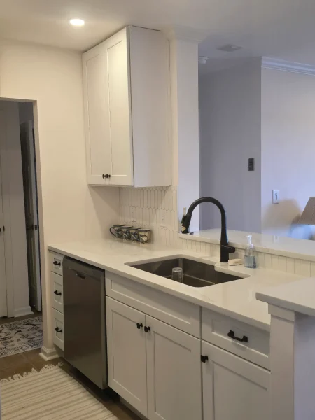 White kitchen with an island, black gooseneck faucet, and stainless dishwasher beneath light gray countertops and white cabinets.