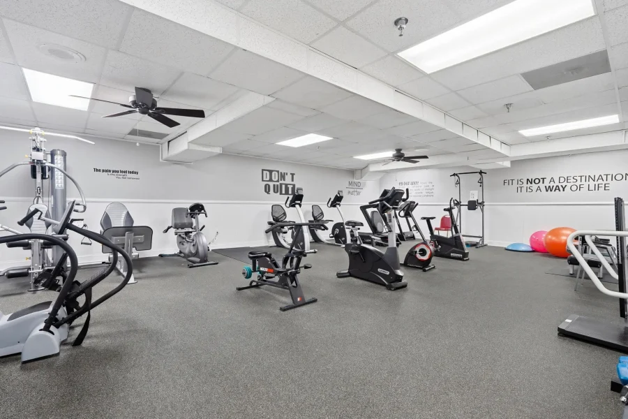 A spacious gym with cardio machines (ellipticals and treadmills) and motivational wall quotes like “DON'T QUIT” along the back wall.