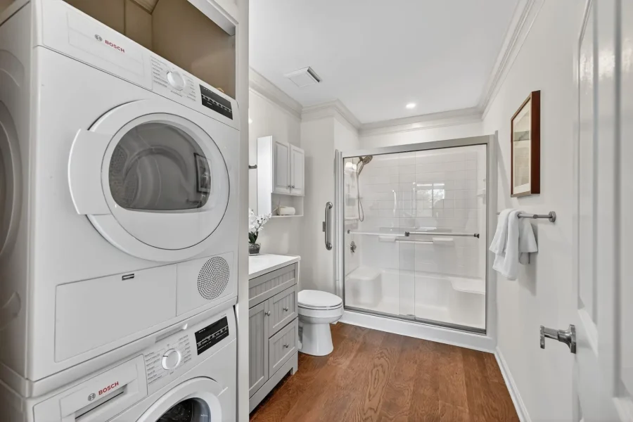 Stacked washer and dryer beside a gray vanity in a small bathroom with a glass shower enclosure.