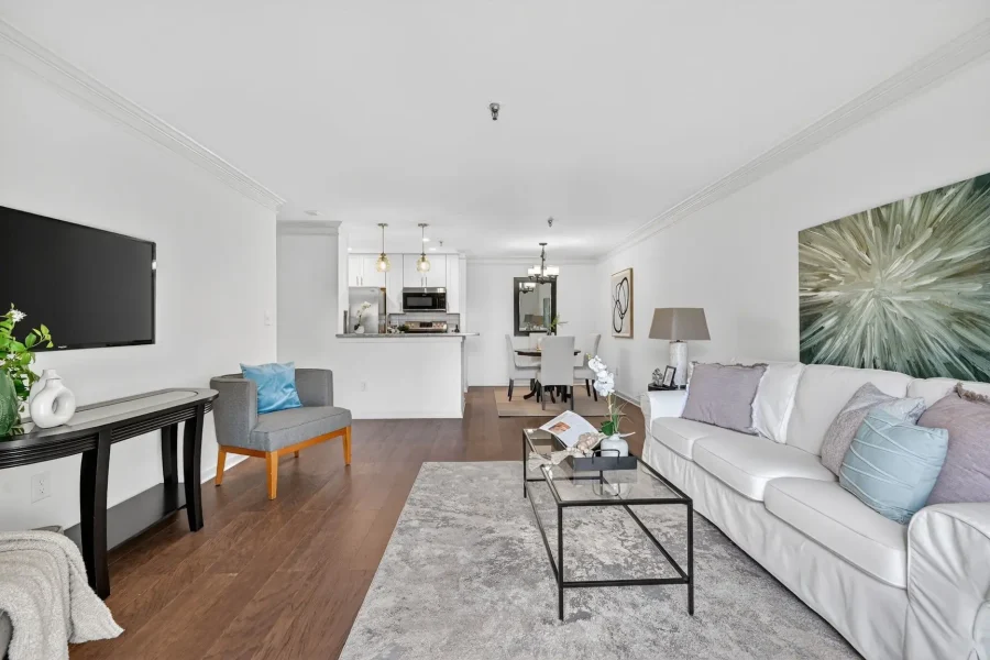Open-concept living room with a white sectional sofa, gray chairs, large abstract green wall art, and a glass coffee table on a gray rug.