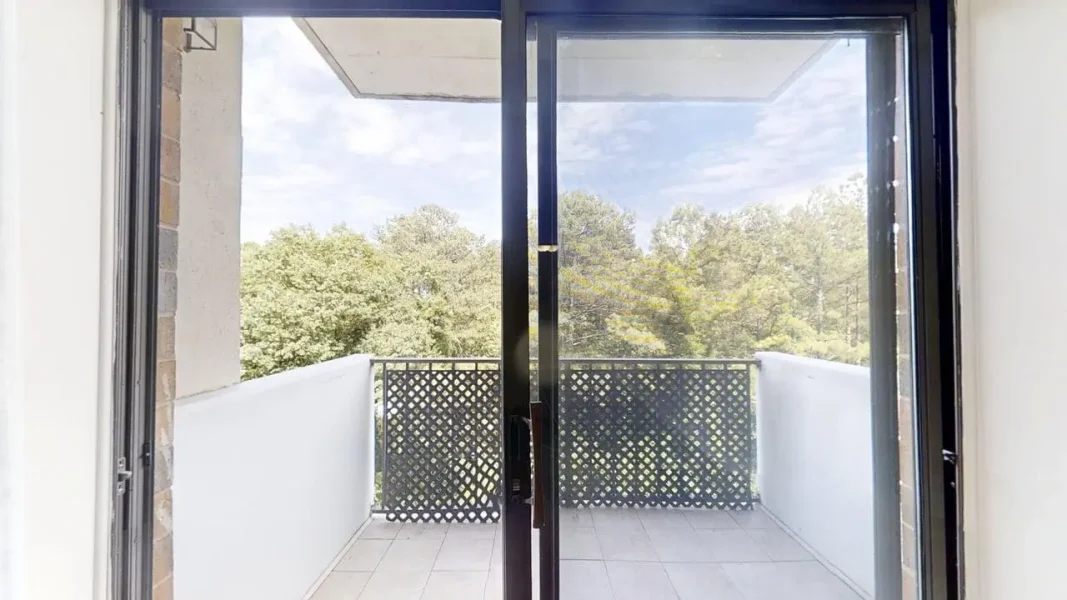 Open glass doors leading to a small balcony with a lattice railing and trees beyond.