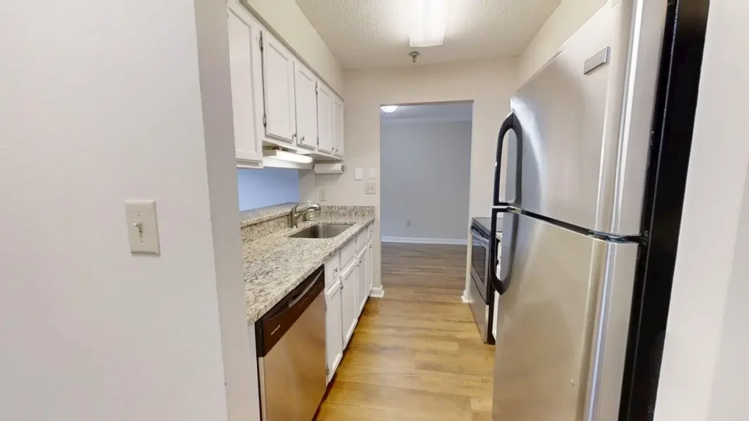 Galley kitchen with white cabinets, granite counters, and stainless steel fridge and dishwasher.