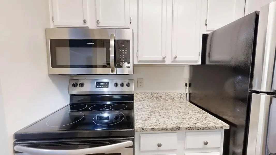 Stainless steel microwave above a glass-top electric range in a white kitchen with a granite counter.