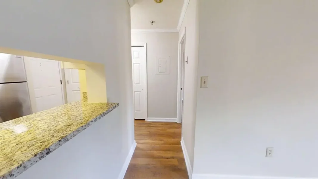 Hallway view from a kitchen bar with granite counter, leading to white doors and hardwood floor.