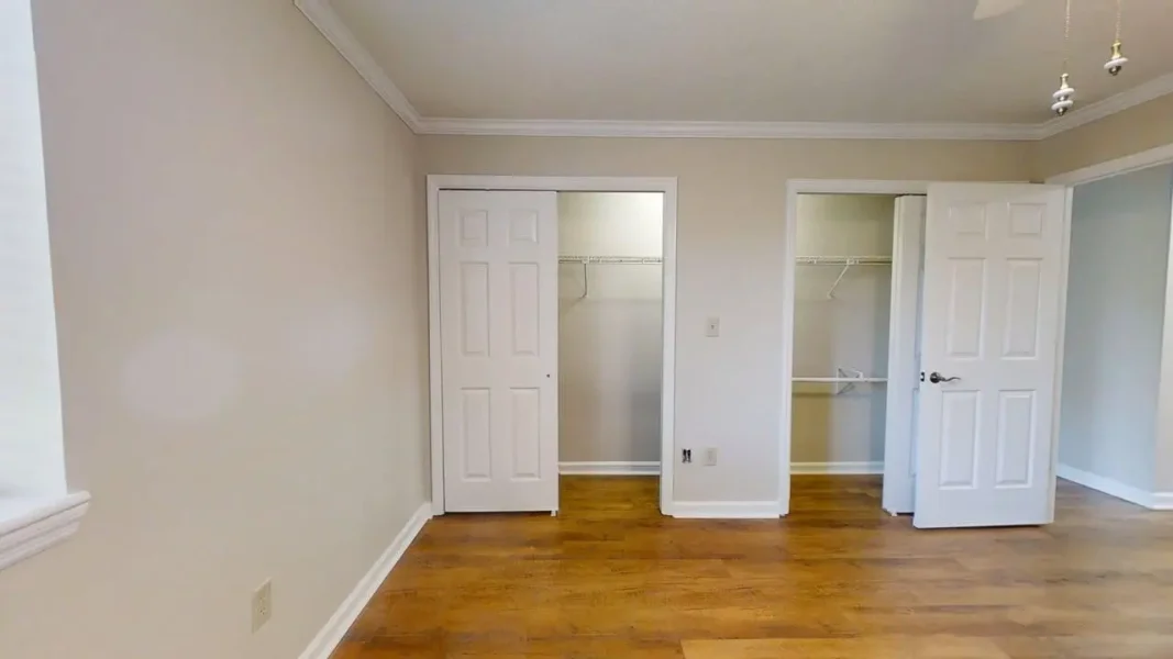 Empty room with hardwood floor, beige walls, white baseboards, and two open closets with wire shelves inside.