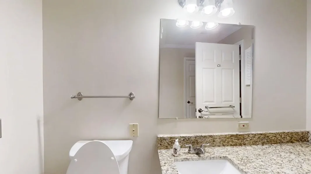 Bathroom vanity with granite countertop, sink and faucet, large mirror, and a door reflected in the mirror