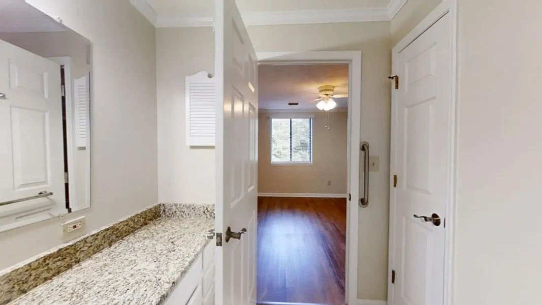View from a bathroom vanity into a room with hardwood floor and a ceiling fan in the distance.