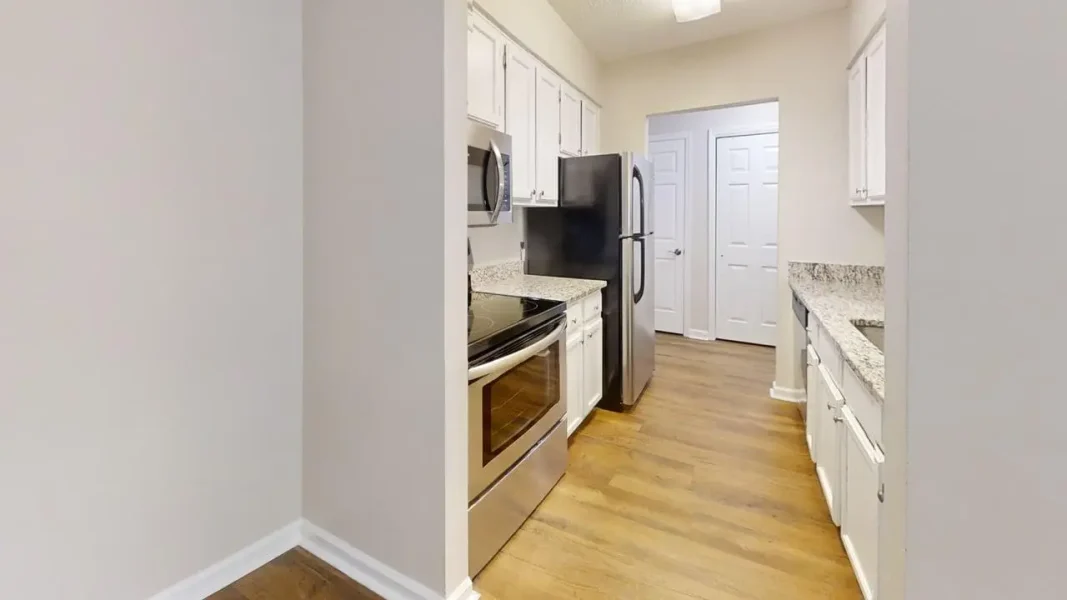 Modern kitchen with white cabinets, granite countertops, and stainless steel refrigerator, stove, and microwave on a light wood floor.