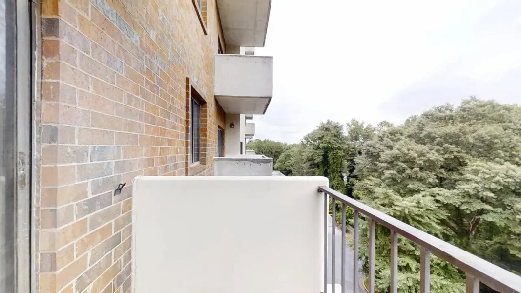 Balcony of a brick apartment building overlooking a tree-lined street below.