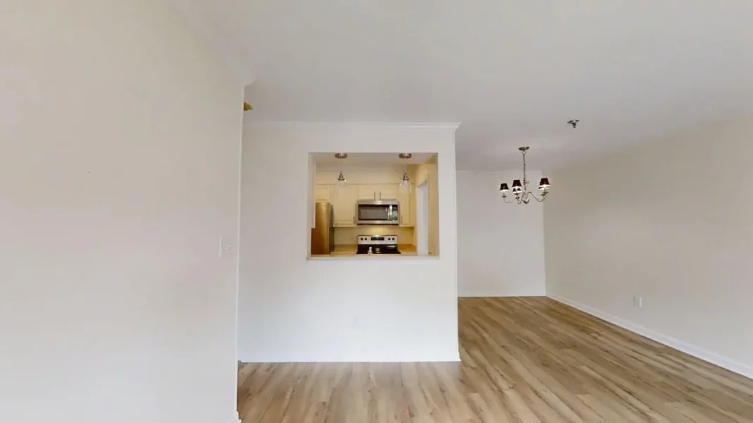 Open-concept living area with a pass-through window to the white kitchen, wood-look flooring, and a chandelier overhead.