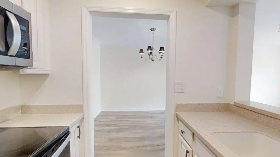 Kitchen with white cabinets, speckled countertops, and a doorway to a dining room with a chandelier visible beyond.