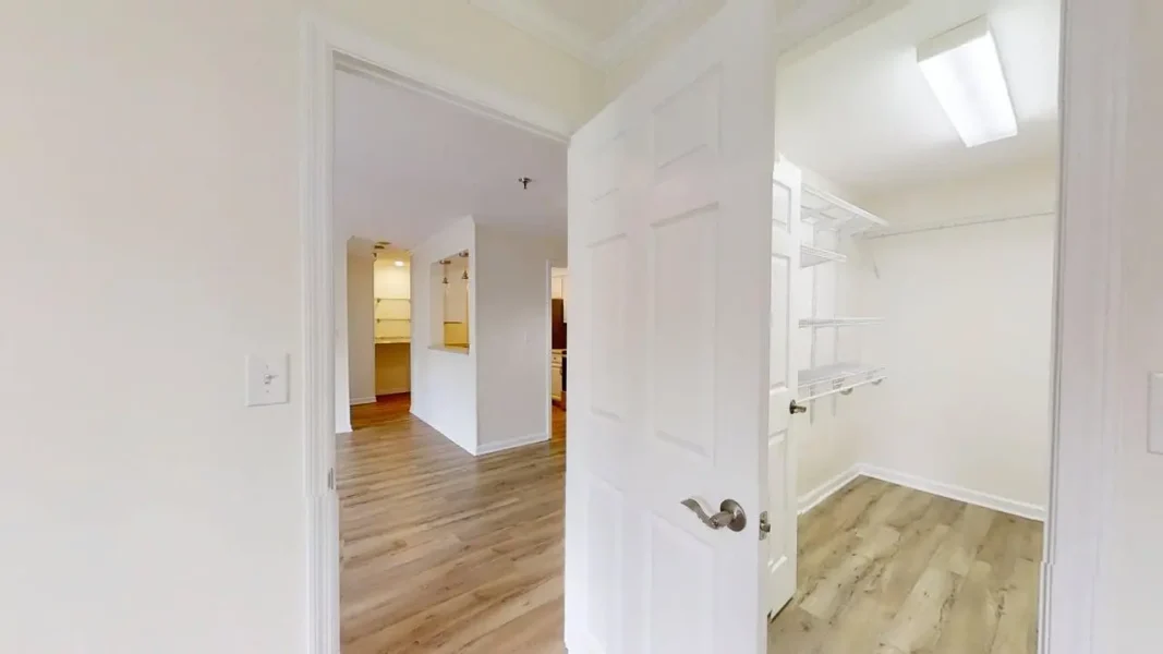 Bright hallway leading to a kitchen with open shelves visible through a doorway. A walk-in closet with white wire shelving is on the right.