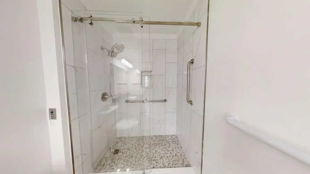 Accessible glass-enclosed shower with grab bars, a handheld showerhead, and a pebble-textured floor.