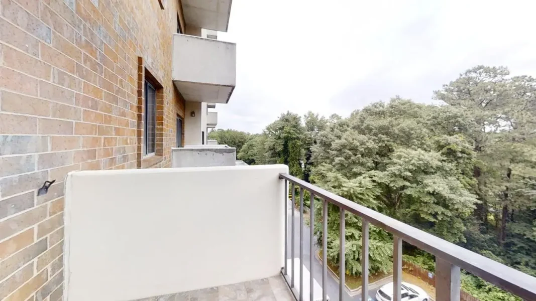 Balcony of a brick apartment building with a metal railing, overlooking a tree-lined street below.