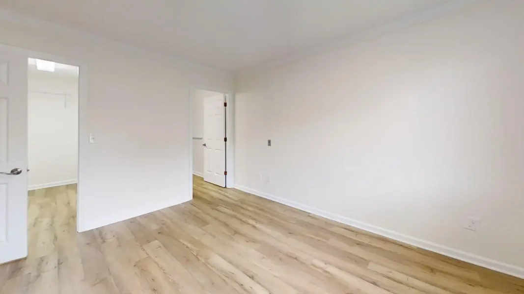 Empty white room with light wood laminate flooring and two white doors, one partially open.
