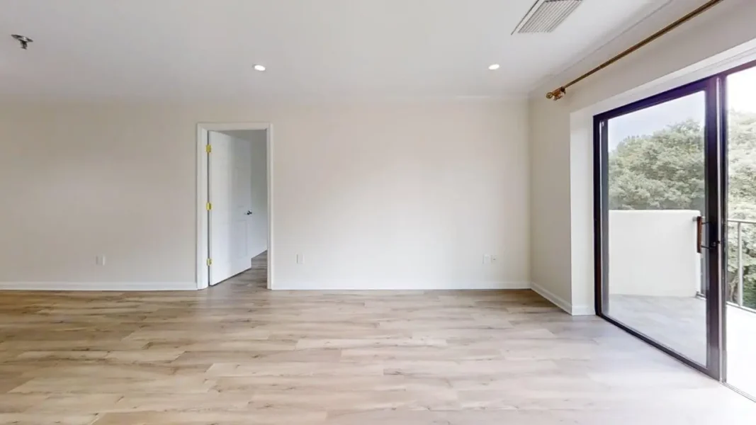 Empty living room with light wood floors, white walls, and a large glass door to a balcony.