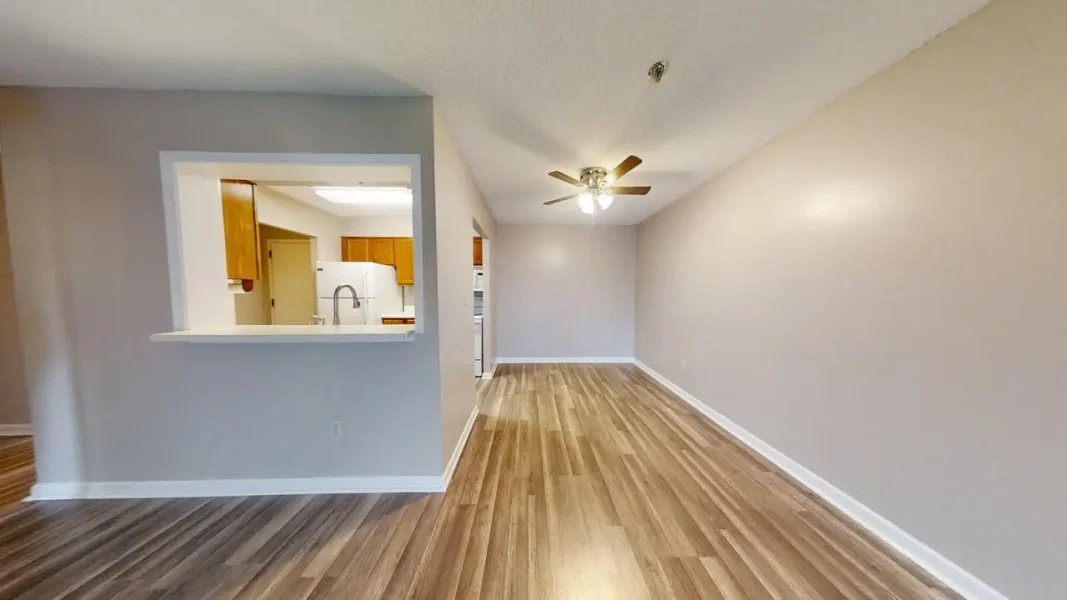 Open-concept living area with a pass-through to the kitchen, wood-look flooring, and a ceiling fan in neutral-toned walls
