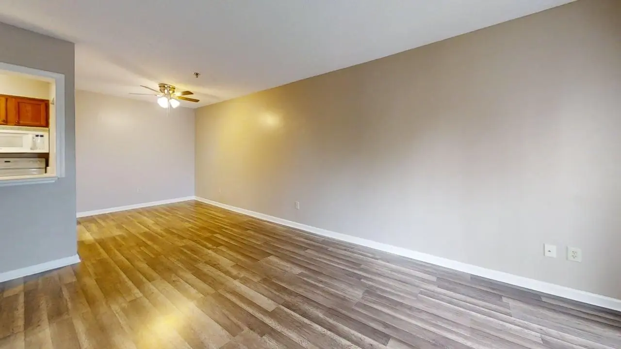 Open-concept living room and kitchen: beige sofa, granite-topped breakfast bar, and stainless-steel appliances with hardwood floors.