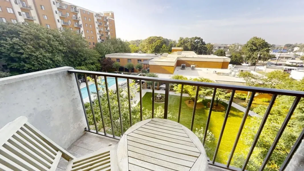 Balcony view overlooking a courtyard with a pool, trees, and surrounding low-rise buildings.