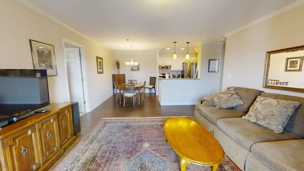 Open-concept living room with a beige sofa, wooden coffee table, and rug, opening to a dining area and kitchen.