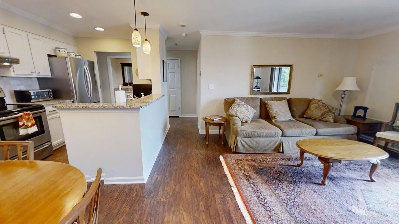 Open-concept living room and kitchen: beige sofa, granite-topped breakfast bar, and stainless-steel appliances with hardwood floors.