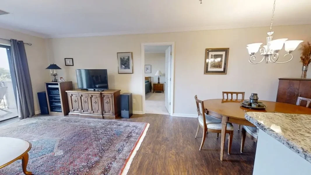 Living room with TV on a wooden cabinet, tall speakers, and a patterned area rug; sliding glass door to a balcony on the left.