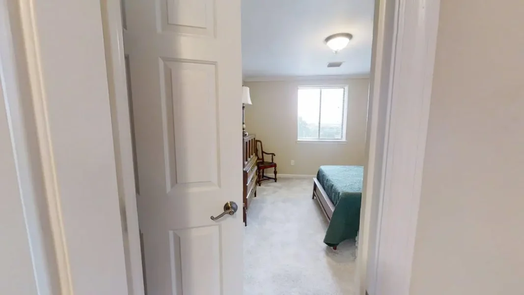 Bedroom viewed from doorway: bed with teal cover on the right, wooden dresser and chair against the left wall, window near the far wall.
