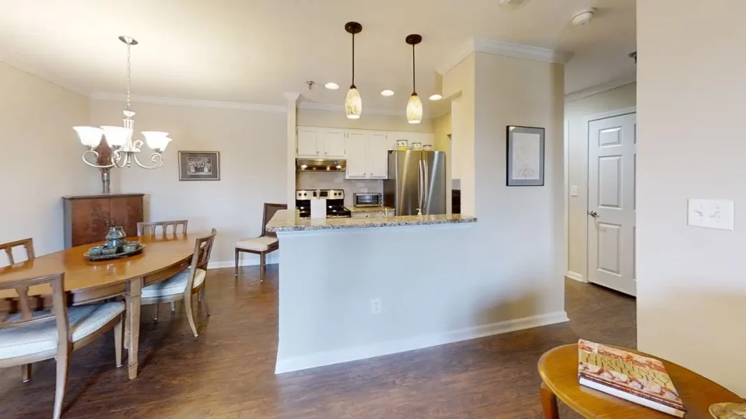 Open-concept kitchen and dining area with a granite breakfast bar, pendant lights, wooden dining table, and stainless steel appliances.