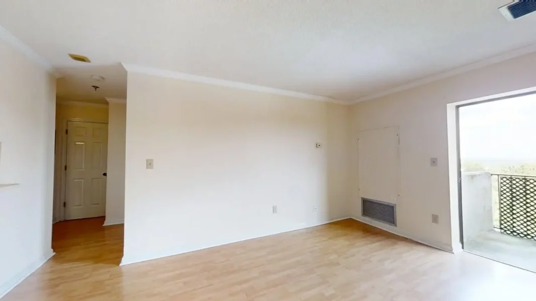 Empty living room with light wood floors, white walls, and a sliding glass door opening to a balcony on the right.