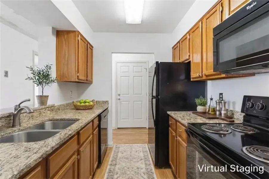 Modern galley kitchen with wooden cabinets, granite counters, and black appliances (refrigerator, stove) with a sink and plant on the counter.