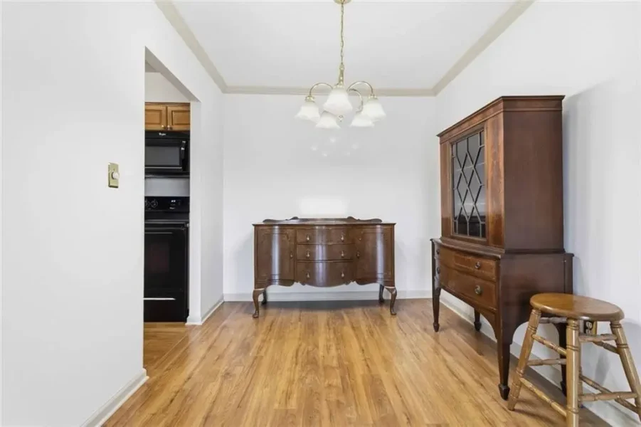 Dining room with antique wooden sideboard, china cabinet, and a stool on a hardwood floor under a hanging chandelier.