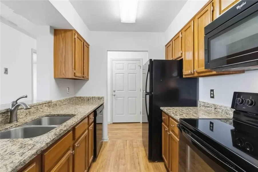 U-shaped kitchen with granite counters, oak cabinets, a double sink, and black appliances (fridge, stove, microwave).