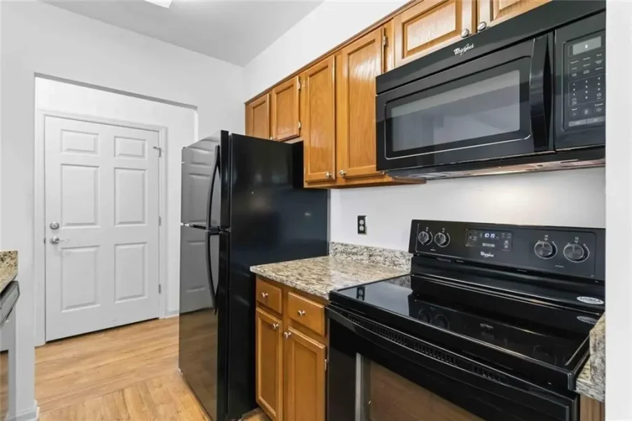 Kitchen with black refrigerator, stove, and microwave, wooden cabinets, and speckled granite countertops