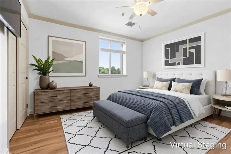 Modern staged bedroom with a king bed, white headboard, blue bedding, bench at the foot, two nightstands with lamps, abstract wall art, and a wooden dresser with plants.