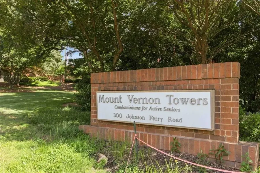 Brick sign for Mount Vernon Towers condominiums for active seniors at 300 Johnson Ferry Road, with green trees in the background.
